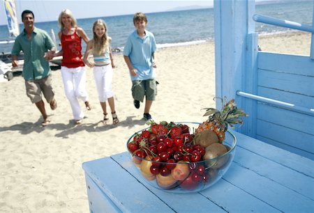 Bowl of fruit and parents with children on beach Stock Photo - Premium Royalty-Free, Code: 644-02060573