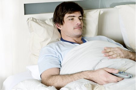 Young man in bed with remote control Stock Photo - Premium Royalty-Free, Code: 644-02923410