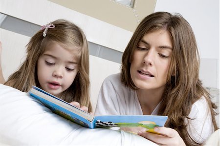 Young woman and girl on bed reading a book Stock Photo - Premium Royalty-Free, Code: 644-02923492