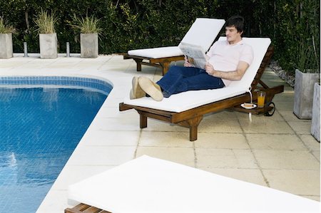 Young man on chaise lounge by pool reading Stock Photo - Premium Royalty-Free, Code: 644-02923542