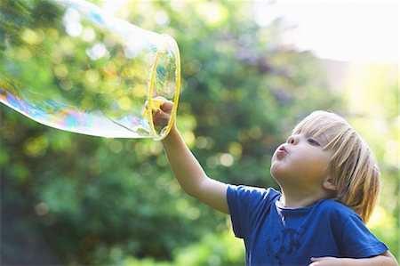 exhaling - Boy blowing oversized bubble in backyard Stock Photo - Premium Royalty-Free, Code: 649-04247853