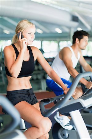 Woman on cell phone on exercise machine Stock Photo - Premium Royalty-Free, Code: 649-05950195