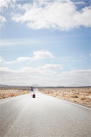 future of the desert - Woman rolling luggage on rural road Stock Photo - Premium Royalty-Free, Code: 649-05950792