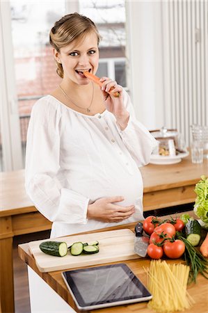 photograph of pregnant women - Femme enceinte mange des carottes dans la cuisine Photographie de stock - Premium Libres de Droits, Code: 649-06000455