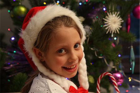 santa claus hat - Girl wearing Santa hat by Christmas tree Stock Photo - Premium Royalty-Free, Code: 649-06532747