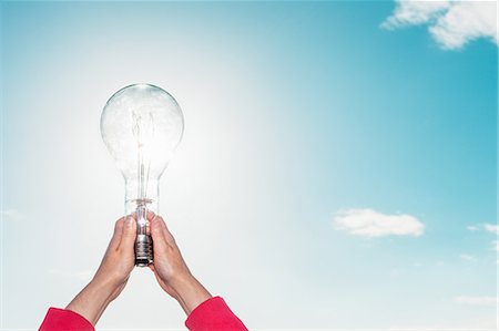 energy concept - Woman holding light bulb in sky Stock Photo - Premium Royalty-Free, Code: 649-06716896