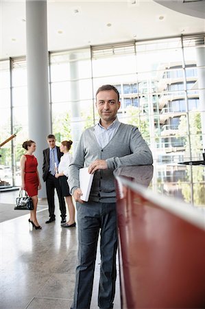 Businessman holding laptop leaning against reception desk Stock Photo - Premium Royalty-Free, Code: 649-06812114