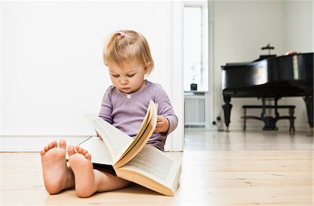 Toddler girl sitting on floor reading book Stock Photo - Premium Royalty-Free, Code: 649-06812255