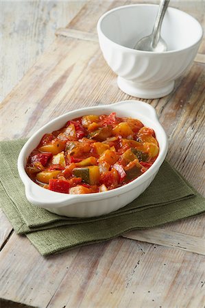 Vegetable ratatouille. Courgettes, tomatoes and red and yellow peppers in white dish on a green cloth Stock Photo - Premium Royalty-Free, Code: 649-06812342