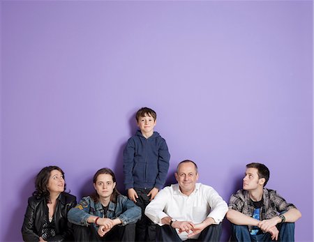 Boy standing in the middle of sitting family in front of purple background Stock Photo - Premium Royalty-Free, Code: 649-06829583