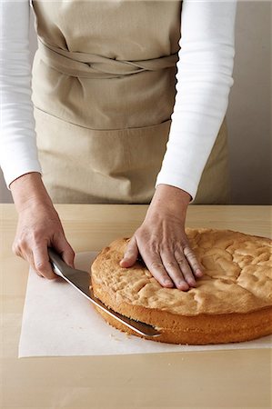 Woman slicing top off sponge cake Stock Photo - Premium Royalty-Free, Code: 649-06830085