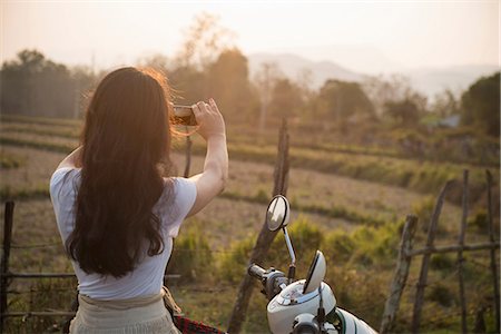 Woman on moped taking photograph in rural scene Stock Photo - Premium Royalty-Free, Code: 649-06844507