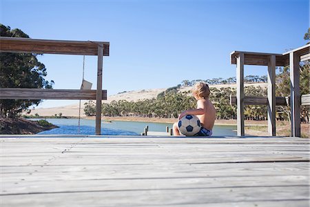 Boy sitting on pier with football Stock Photo - Premium Royalty-Free, Code: 649-06844657