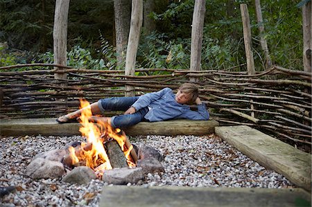 Boy relaxing by fire outdoors Stock Photo - Premium Royalty-Free, Code: 649-06943768