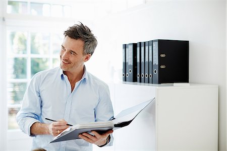 smiling portrait looking away - Man looking at folder of paperwork Photographie de stock - Premium Libres de Droits, Code: 649-07064548