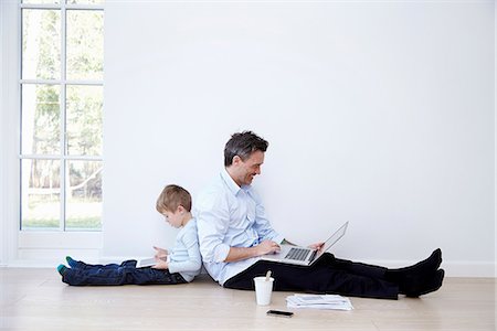 family home indoors - Father and son sitting back to back using laptop and digital tablet Stock Photo - Premium Royalty-Free, Code: 649-07064559