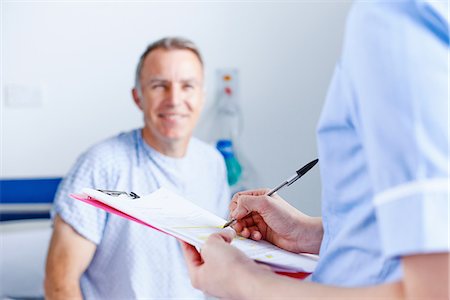 patient and care - Nurse completing paperwork, patient in background Stock Photo - Premium Royalty-Free, Code: 649-07064704