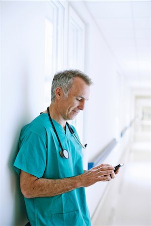 simsearch:649-07064718,k - Surgeon standing in corridor looking at smartphone Stock Photo - Premium Royalty-Free, Code: 649-07064715