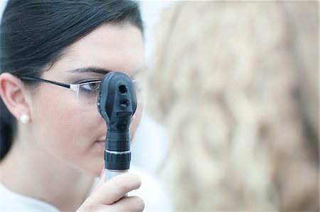 simsearch:649-07063763,k - Female optician looking through ophthalmoscope Stock Photo - Premium Royalty-Free, Code: 649-07063780