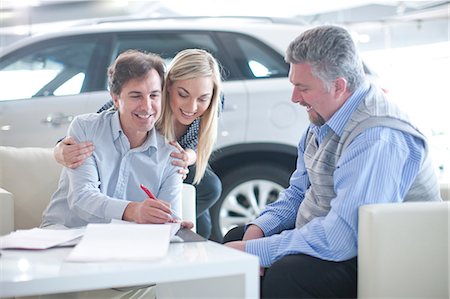 salesman customer car showroom - Car salesman and couple signing contract in car showroom Stock Photo - Premium Royalty-Free, Code: 649-07119149