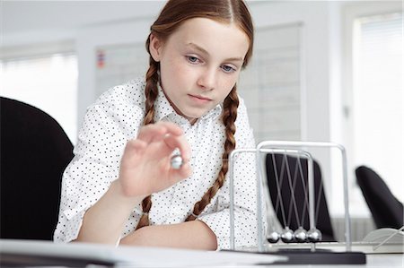 Girl playing with newton's cradle on desk Stock Photo - Premium Royalty-Free, Code: 649-07119788