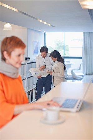 simsearch:649-07238396,k - Businesswoman sitting at table using laptop, colleagues looking at folder in background Stock Photo - Premium Royalty-Free, Code: 649-07238414