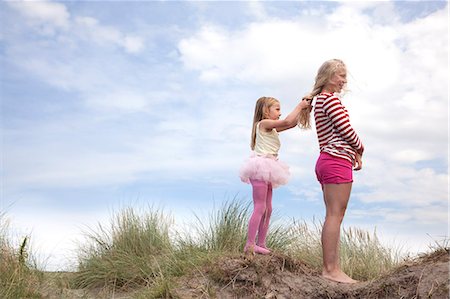 Two girls on dunes, one plaiting friend's hair, Wales, UK Stock Photo - Premium Royalty-Free, Code: 649-07239486