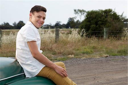 Portrait of young man sitting on bonnet of vintage morris minor Stock Photo - Premium Royalty-Free, Code: 649-07520614