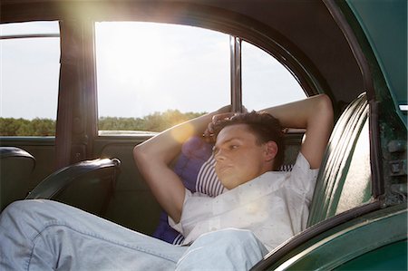 Young man posing in back seat of vintage morris minor Stock Photo - Premium Royalty-Free, Code: 649-07520613