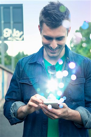 simsearch:649-07560130,k - Young man texting on smartphone with glowing lights coming out of it Stock Photo - Premium Royalty-Free, Code: 649-07560148