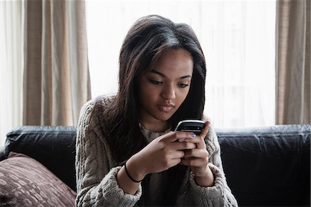 Teenage girl sitting on sofa texting on smartphone Photographie de stock - Premium Libres de Droits, Code: 649-07596197