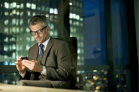 Businessman working late texting on smartphone Fotografie stock - Premium Royalty-Free, Codice: 649-07596249