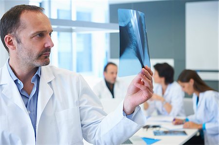 Male doctor looking at x-ray, colleagues having discussion behind Stock Photo - Premium Royalty-Free, Code: 649-07761038
