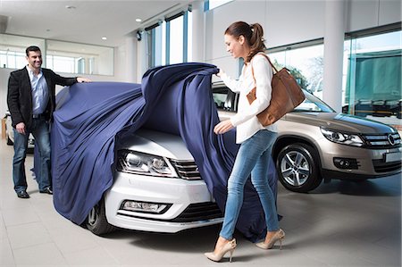 Woman uncovering new car with boyfriend in car dealership Stock Photo - Premium Royalty-Free, Code: 649-07761172