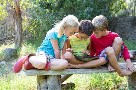 simsearch:649-07804176,k - Three children sitting on garden seat looking down at digital tablet Stock Photo - Premium Royalty-Free, Code: 649-07804159