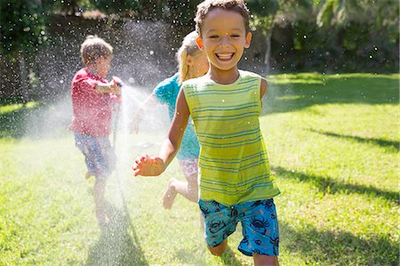 simsearch:649-08180244,k - Three children chasing each other in garden with water sprinkler Stock Photo - Premium Royalty-Free, Code: 649-07804176
