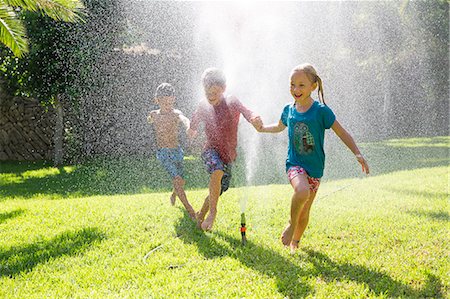 Three children in garden running through water sprinkler Stock Photo - Premium Royalty-Free, Code: 649-07804179
