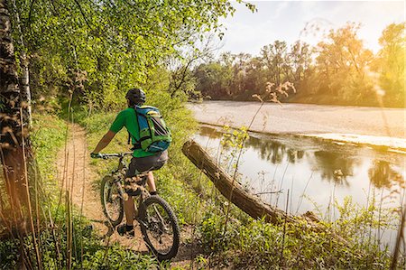 Rear view of young man cycling along riverside path Stock Photo - Premium Royalty-Free, Code: 649-07804658