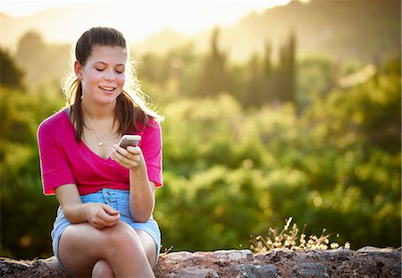 simsearch:649-07804673,k - Teenage girl sitting on stone wall looking at smartphone, Majorca, Spain Photographie de stock - Premium Libres de Droits, Code: 649-07804672