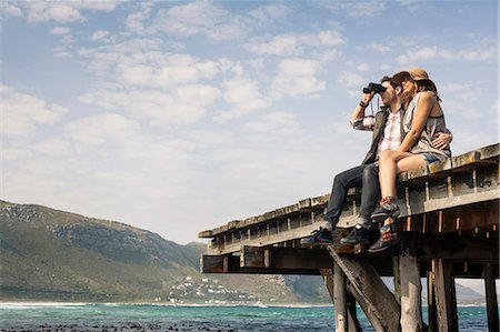 sharing - Young couple sitting on edge of old pier looking through binoculars, Cape Town, Western Cape, South Africa Stock Photo - Premium Royalty-Free, Code: 649-07803295