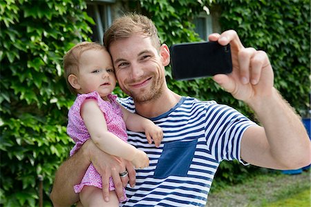 simsearch:649-07804673,k - Mid adult man with baby daughter taking selfie on smartphone  in garden Photographie de stock - Premium Libres de Droits, Code: 649-07803434