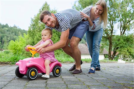 daughter with dad in home - Mid adult couple pushing baby daughter on toy car  in garden Stock Photo - Premium Royalty-Free, Code: 649-07803432