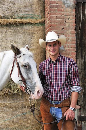 simsearch:649-07560533,k - Portrait of young man in cowboy gear with horse outside stable Photographie de stock - Premium Libres de Droits, Code: 649-07803713