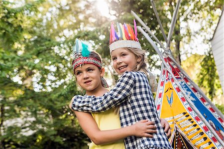 Two girls in native American headdress hugging in garden Stock Photo - Premium Royalty-Free, Code: 649-08060360