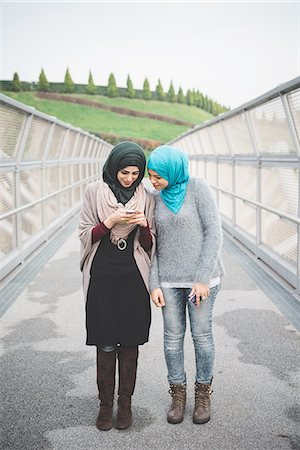 Two young female friends reading smartphone texts on park footbridge Stock Photo - Premium Royalty-Free, Code: 649-08086486