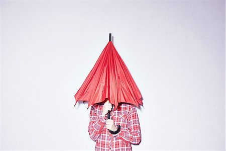 embarrassed women - Studio shot of young woman holding red umbrella over her head Stock Photo - Premium Royalty-Free, Code: 649-08117848
