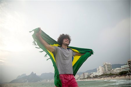 simsearch:649-08117852,k - Smiling young man holding up Brazilian flag on Ipanema beach, Rio De Janeiro, Brazil Foto de stock - Sin royalties Premium, Código: 649-08118402