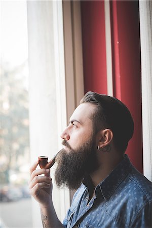 Young bearded man smoking pipe by window Stock Photo - Premium Royalty-Free, Code: 649-08125275