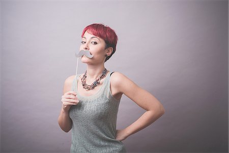 female on gray background - Studio portrait of young woman holding up mustache in front of face Stock Photo - Premium Royalty-Free, Code: 649-08125674