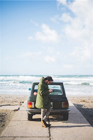 device - Man with vintage car parked on beach reading smartphone texts, Sorso, Sassari, Sardinia, Italy Foto de stock - Sin royalties Premium, Código: 649-08125707